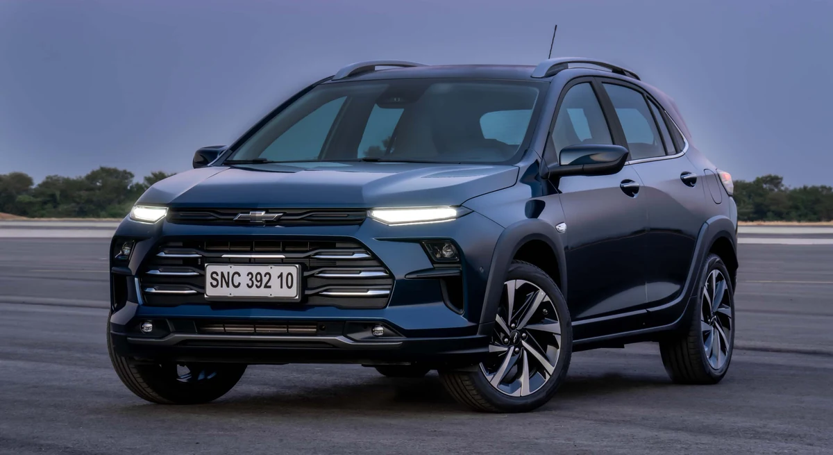 Chevrolet Sonic Premier azul-escuro parado numa pista sob céu de fim de tarde, visto em três quartos dianteiro com os faróis acesos