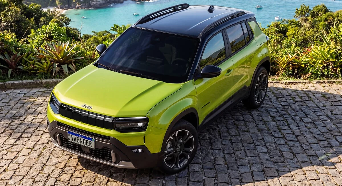 Jeep Avenger verde-limão com teto preto visto de frente em ângulo elevado, estacionado em mirante de pedra diante do mar