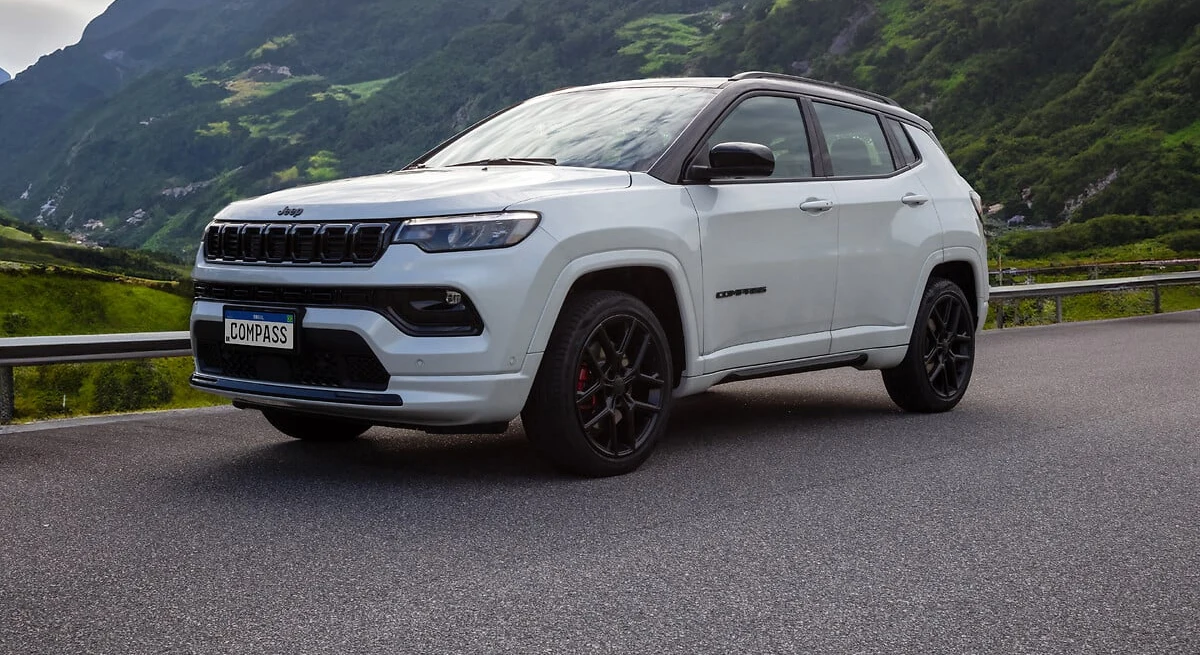 Jeep Compass Blackhawk branco, de teto preto e rodas escuras, parado em estrada de serra com montanhas verdes ao fundo