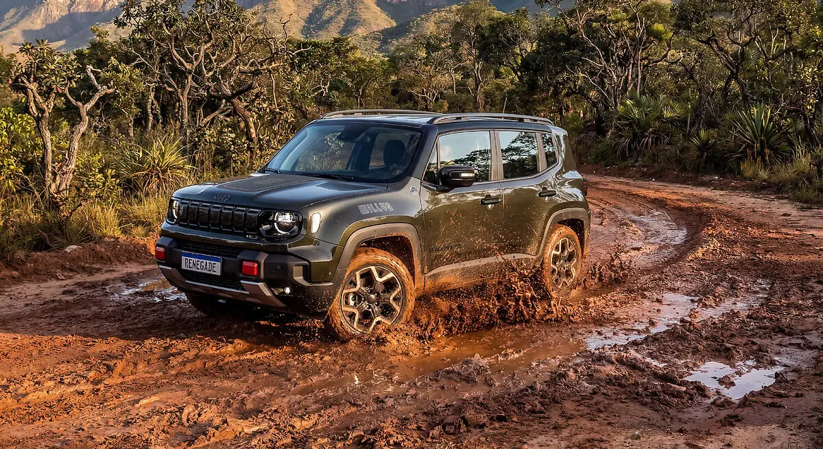 Jeep Renegade Willys 2027 verde-escuro cruzando um trecho de lama em estrada de terra, com montanhas ao fundo