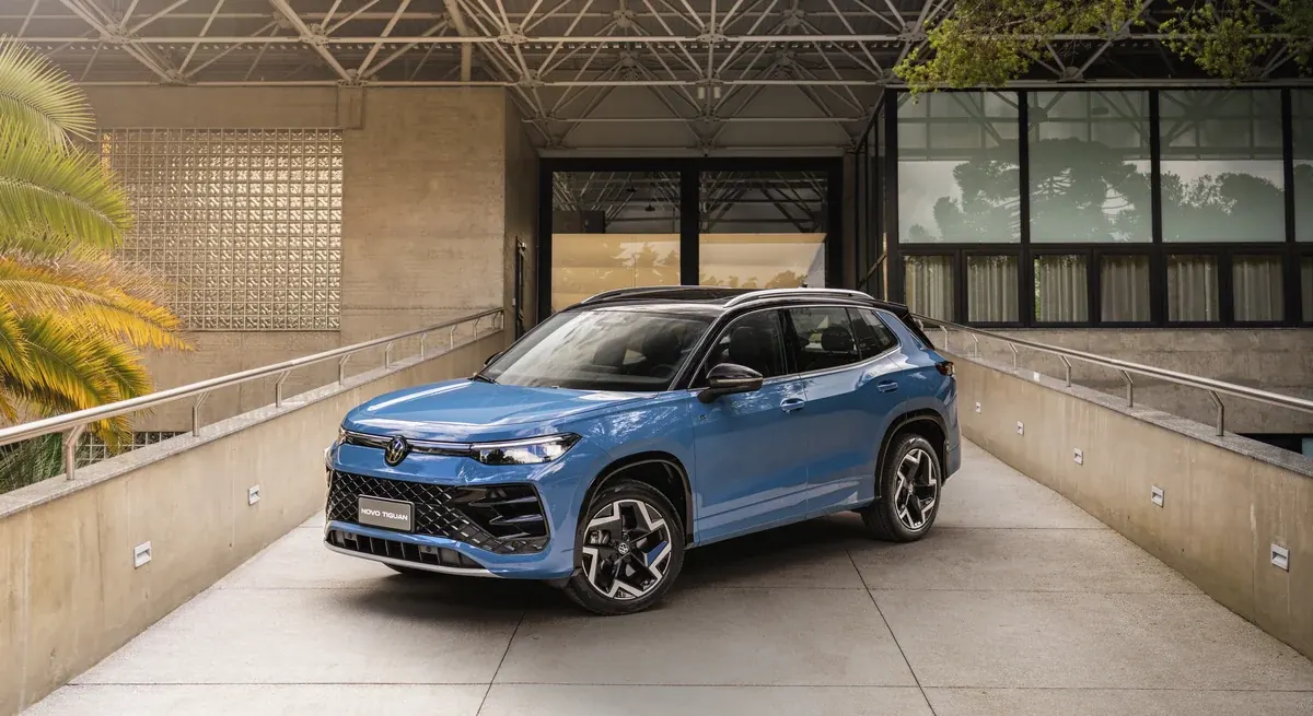 Novo Volkswagen Tiguan R-Line azul visto de três quartos dianteiros, parado numa rampa de concreto entre guarda-corpos, com a inscrição Novo Tiguan na placa do para-choque