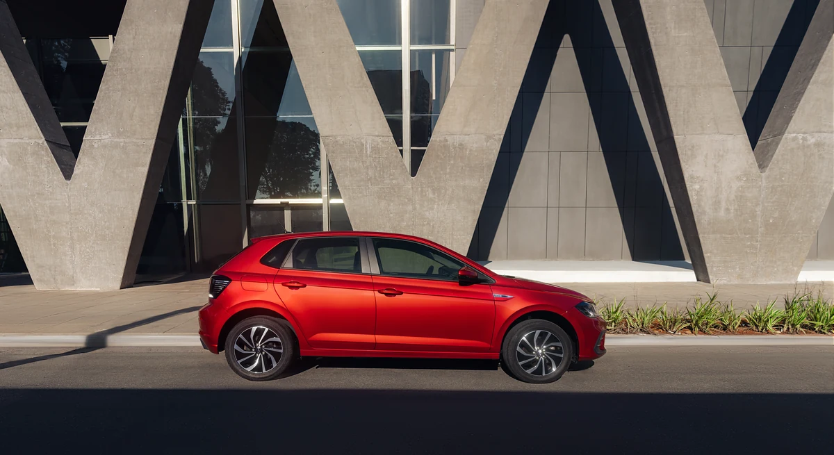 Volkswagen Polo vermelho fotografado de perfil diante de uma fachada arquitetônica clara