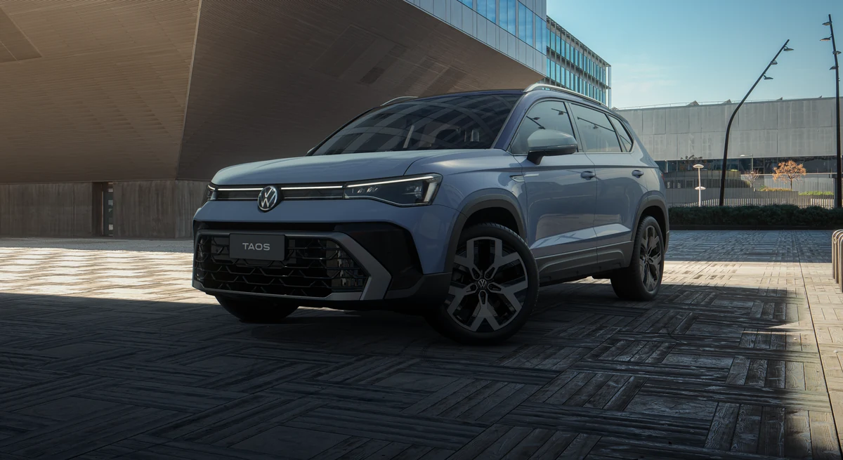 Volkswagen Taos azul da linha nova parado em área urbana ao amanhecer, visto em três quartos dianteiro, com a assinatura de iluminação em X nos faróis