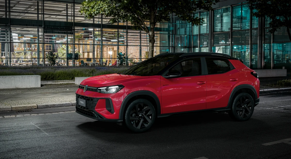 Volkswagen Tera 2027 vermelho parado à noite diante de um prédio envidraçado iluminado, visto em três quartos dianteiro