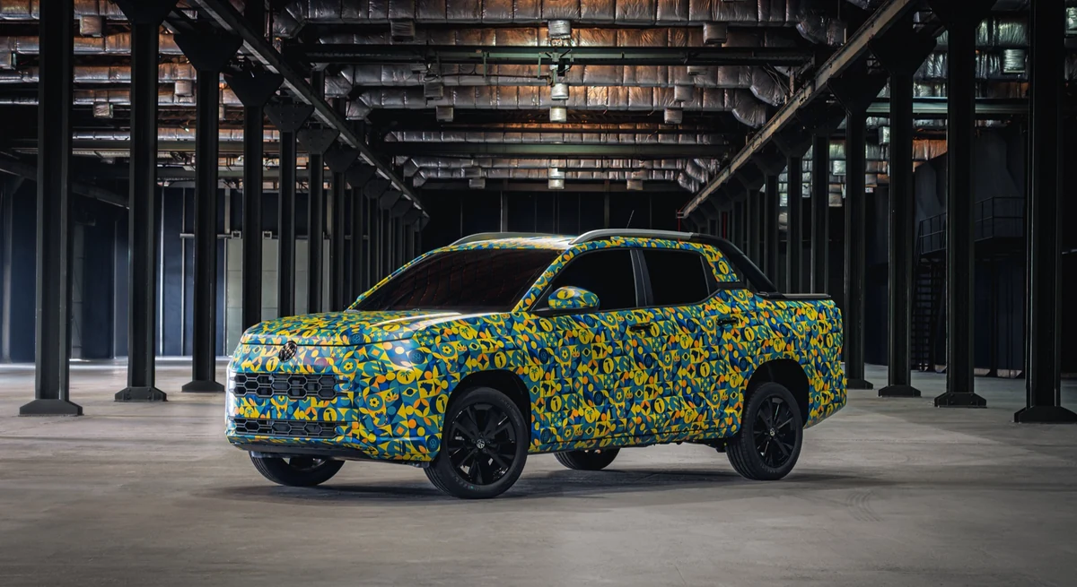 Picape Volkswagen Tukan coberta pela camuflagem artística azul e amarela da apresentação oficial, vista de frente em três quartos dentro de um galpão industrial