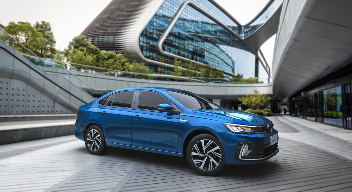 Volkswagen Virtus azul em movimento numa via urbana, visto em três quartos dianteiro, com prédios modernos ao fundo